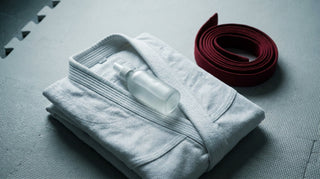 A folded white gi with a skin mist bottle, mat etiquette and cleanliness for beginners