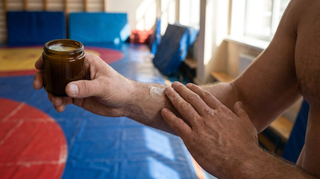 Wrestler applying soothing skin balm to his forearm after wrestling practice